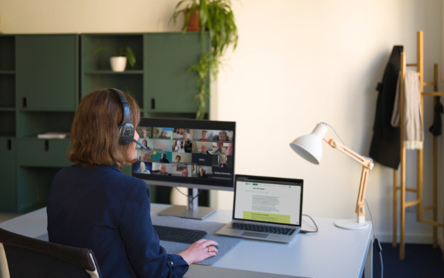 Foto einer Frau die mit Headset am PC sitzt und einen Zoom-Call anleitetet