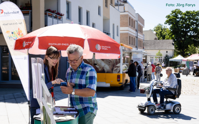 Foto vom Digitalen Engel in Aktion auf einem Marktplatz: Unsere Mobilreferentin erklärt einem Herrn etwas am Handy